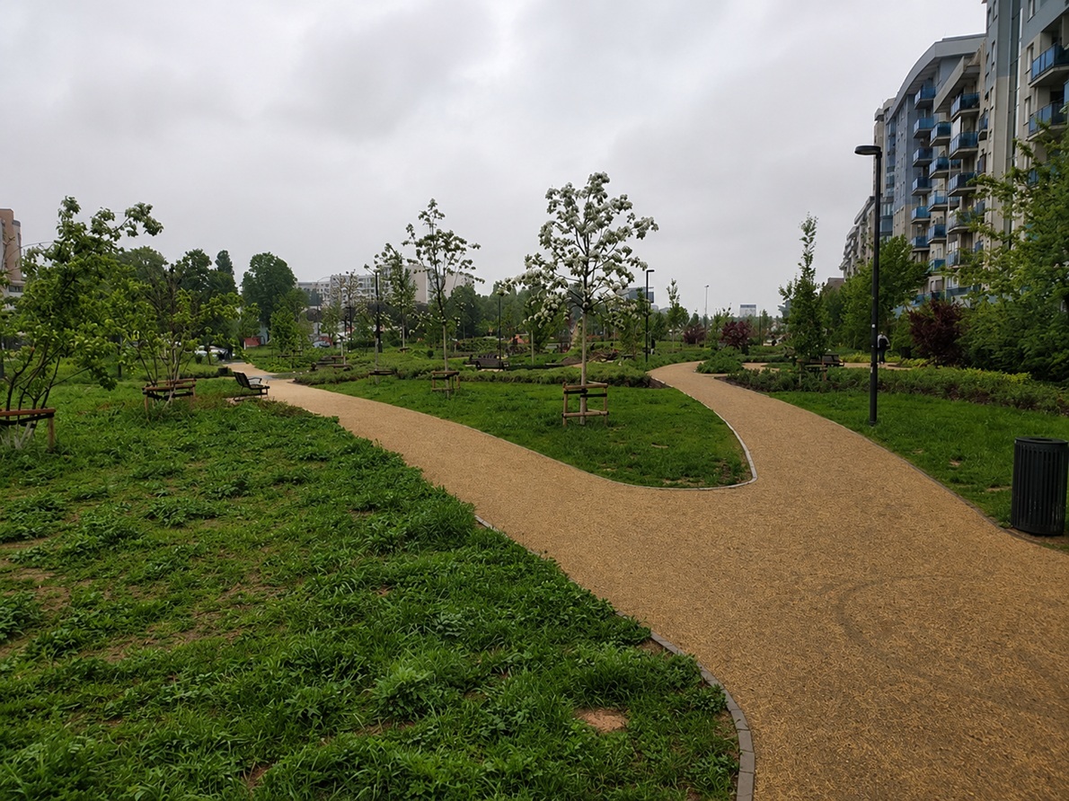 Green linear park with winding walking paths surrounded by apartment buildings in Ursynów, Warsaw — the district's characteristic residential green corridor