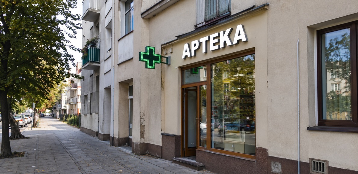Pharmacy storefront in Poland with a green illuminated cross and APTEKA sign